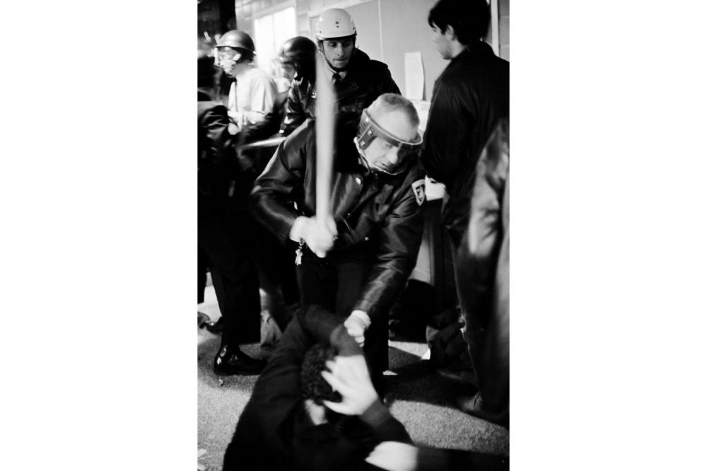 A police officer moves to strike a student on the floor, protecting his head, in the hallway of the Commerce Building.
