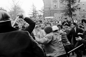  A Madison police officer raises his nightstick during the violent melee, a crowd of angry students in the background on Bascom Hill.