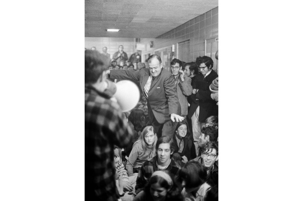 University Police Chief Ralph Hanson tries to make his way through seated student protestors in the hallway of the Commerce Building.