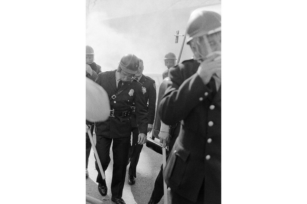 A group of policemen cover their mouths as they walk through a tear gas-filled haze.